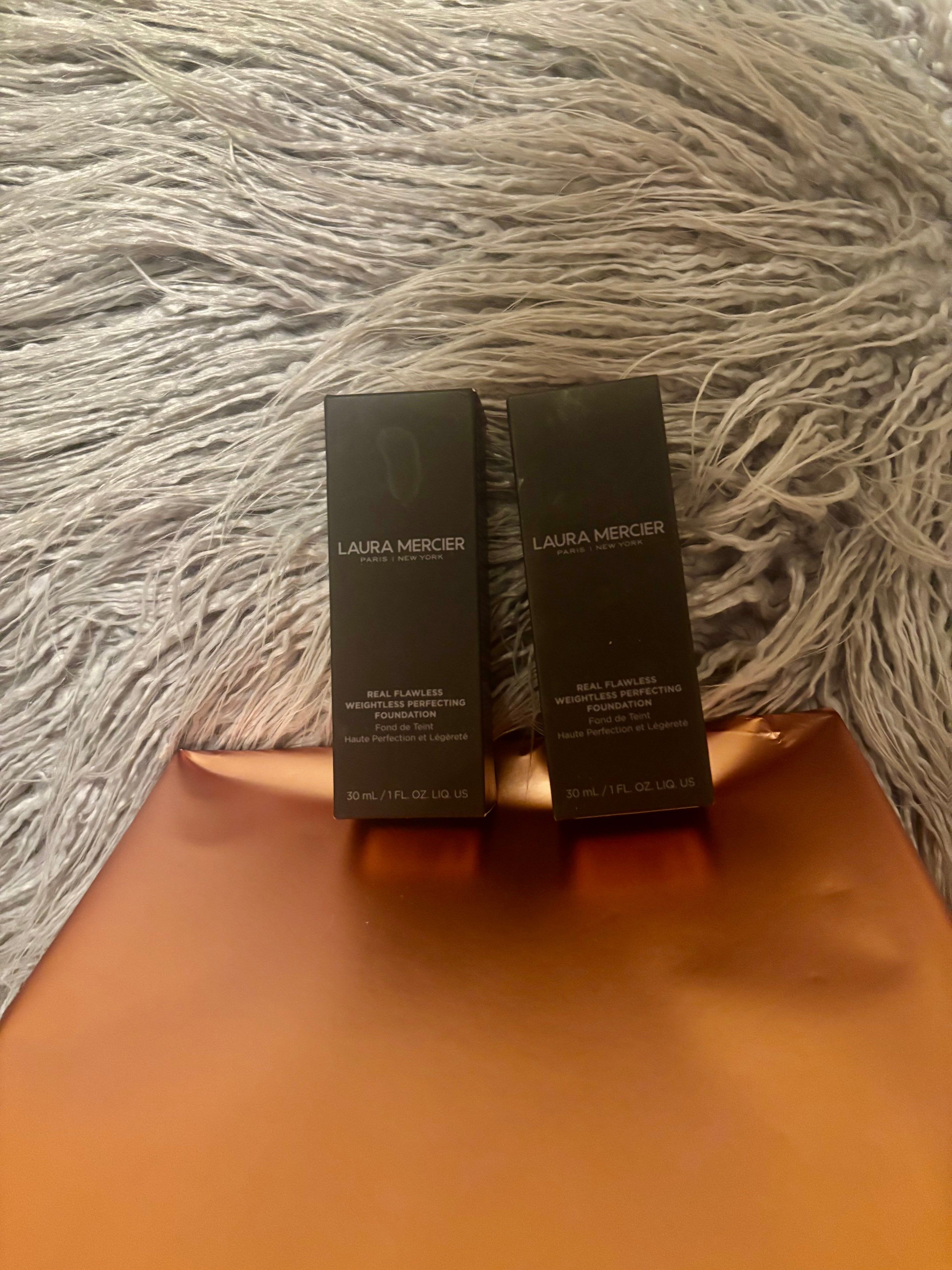 Two Laura Mercier skincare products on a textured surface
