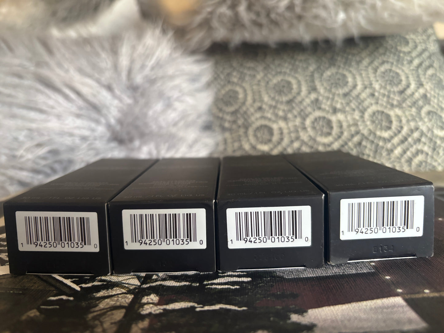 Four black boxes with barcodes on a textured surface Laura Mercier 